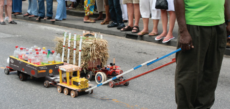 Two Model Tractors with Separate Carts Carrying Canes & Bottles Through the Streets of Holetown at Holetown Festival, St. James, Barbados Pocket Guide
